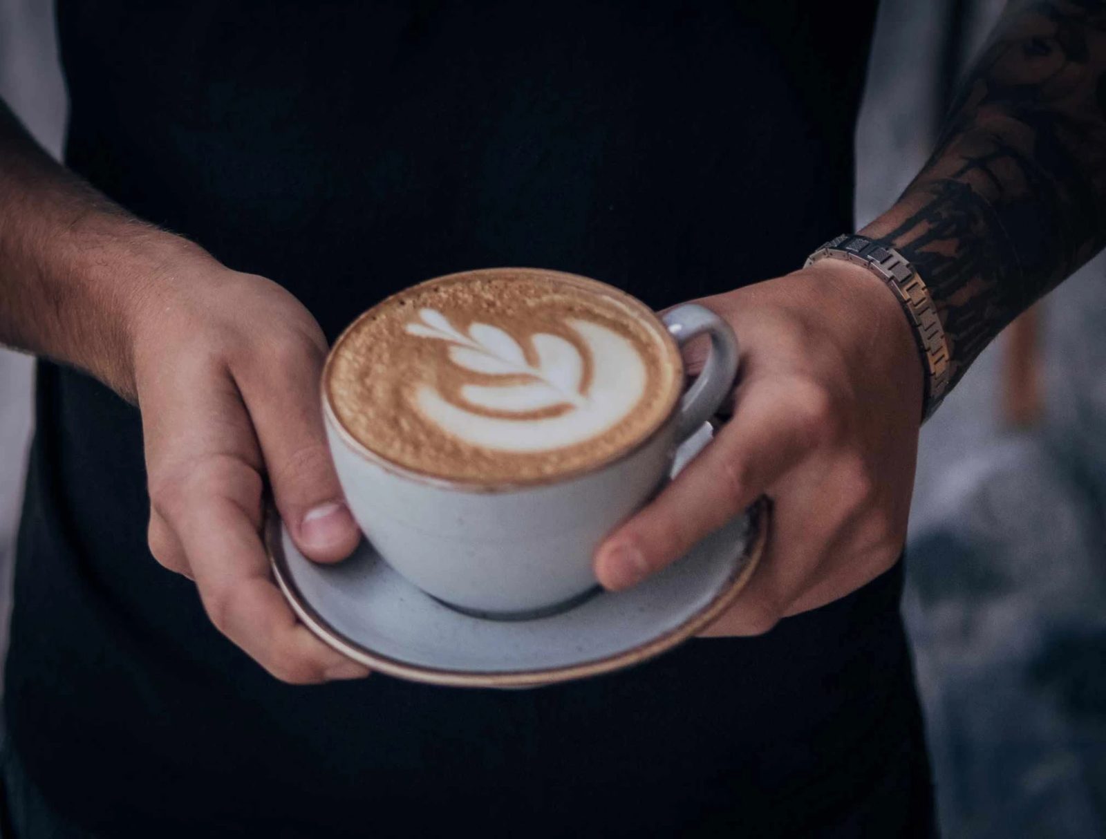 Filiżanka cappuccino z latte art obok suszonego różowego kwiatu na lnianym obrusie